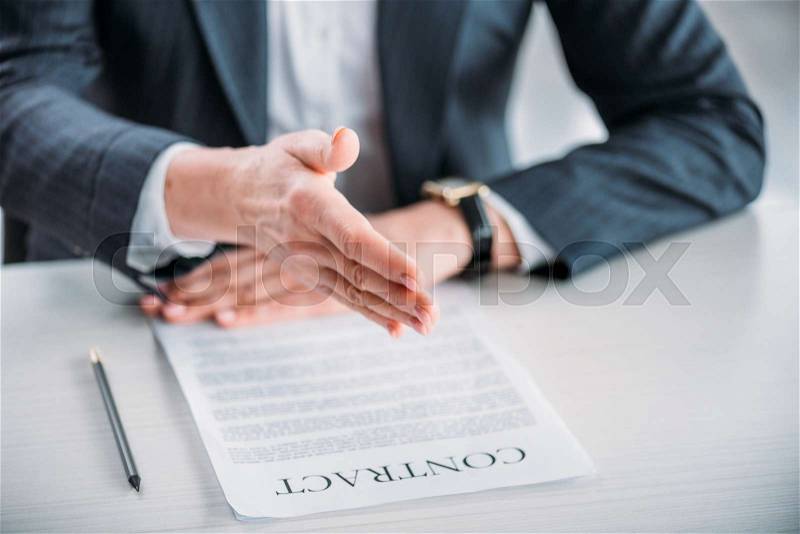 Partial view of businesswoman extending hand for handshake with contract on tabletop, stock photo