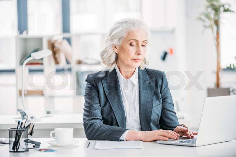 Portrait of confident businesswoman typing on laptop at workplace in modern office, stock photo