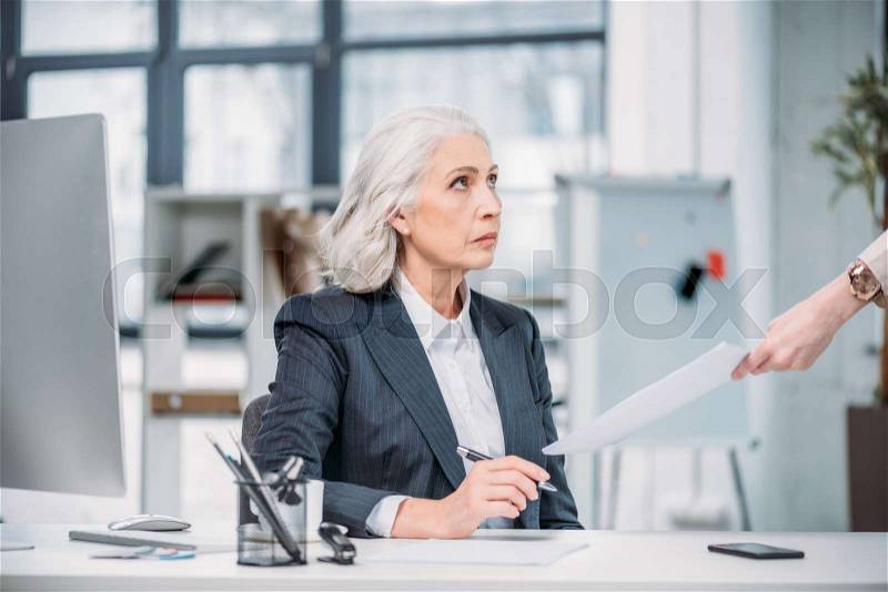 Serious senior businesswoman looking at hand holding paper, stock photo