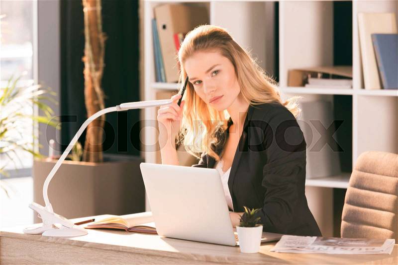 Beautiful young businesswoman using laptop and looking at camera, stock photo