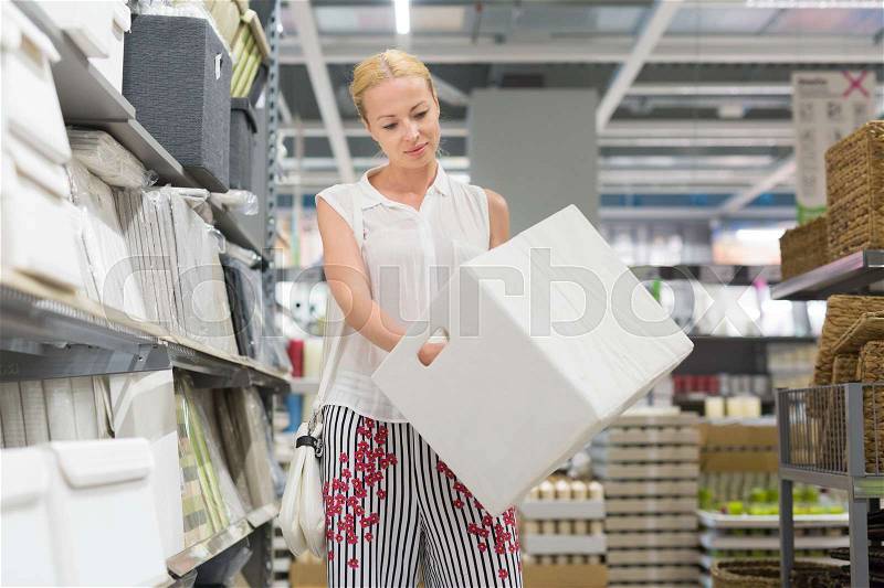 Beautiful young caucasian woman choosing the right item for her apartment in a modern home decor furnishings store. Shopping in retail store, stock photo