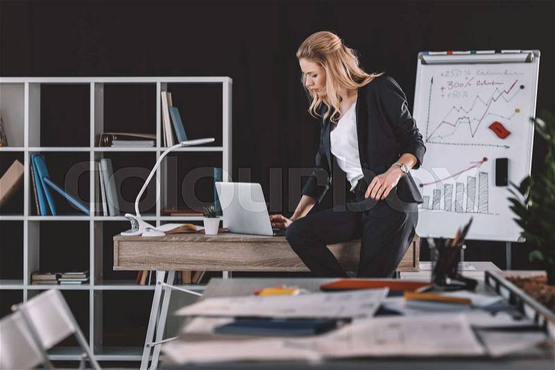 Attractive businesswoman working in office, whiteboard with graphics and charts behind, stock photo