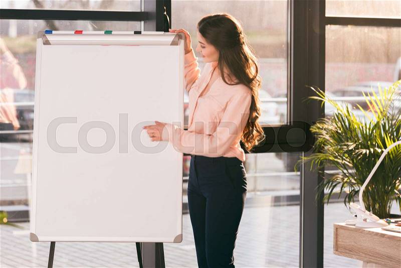 Professional young businesswoman making presentation and pointing at blank whiteboard, stock photo