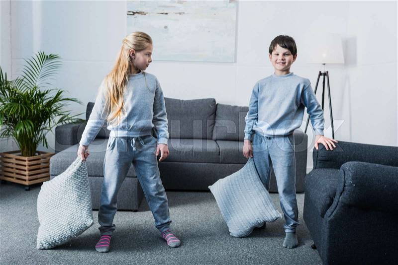 Adorable little children in pajamas having pillow fight at home, stock photo