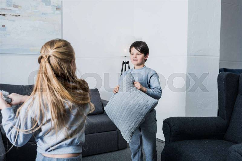 Cute little siblings in pajamas fighting with pillows at home, stock photo