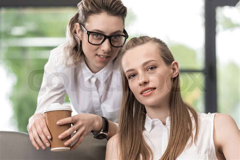 Portrait of stylish woman with coffee to go with girlfriend near by looking at camera, stock photo