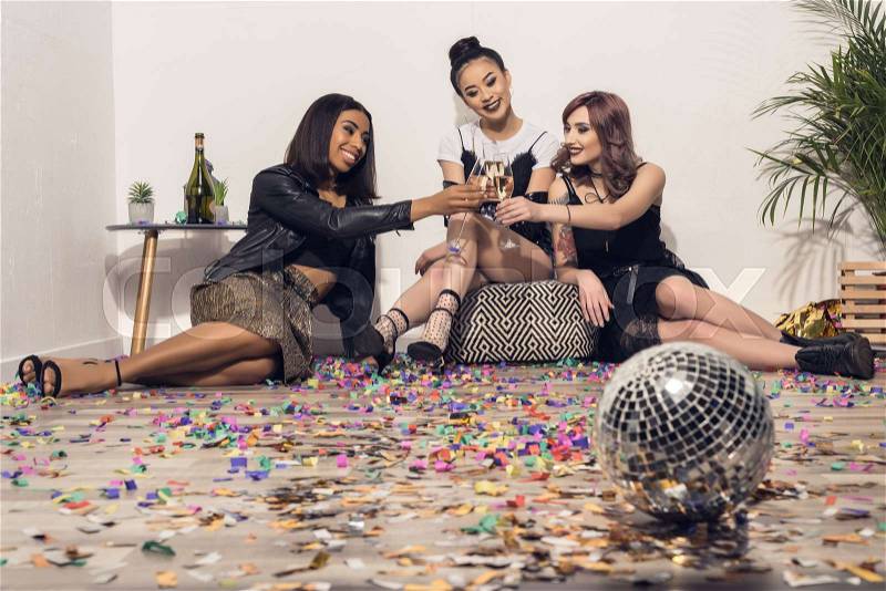 Young happy multiethnic girls sitting and drinking champagne at party, stock photo