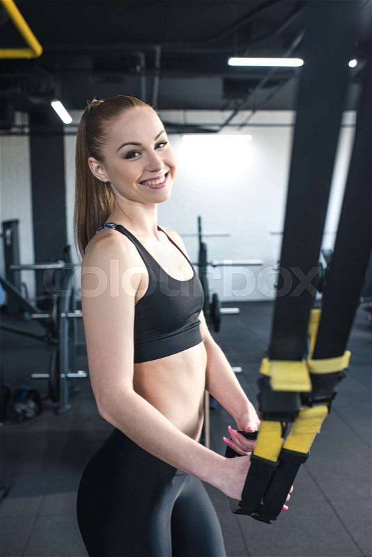 Sportswoman training with trx resistance band in sports center, stock photo