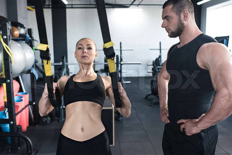 Sportswoman training with trx resistance band with serious trainer in sports center , stock photo