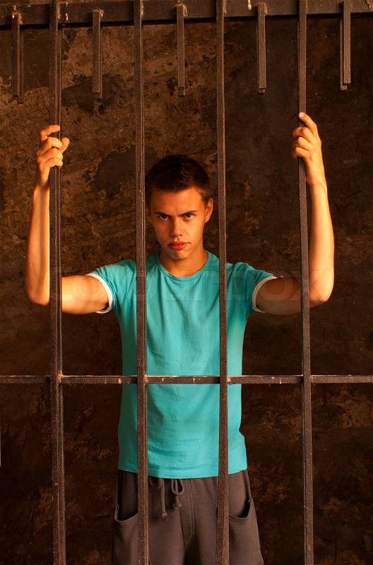 Man with hands tied with rope behind the bars, stock photo