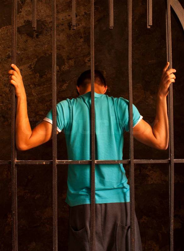 Man with hands tied with rope behind the bars, stock photo