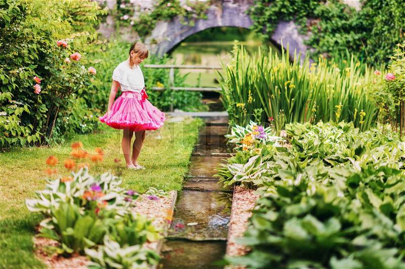 Sweet little girl playing in a small secret garden on a nice summer day, wearing pink tutu skirt, stock photo