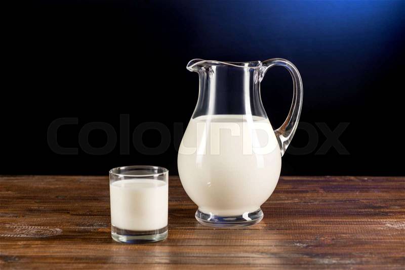 Close-up view of fresh organic milk in glass jug and glass on wooden table top, stock photo