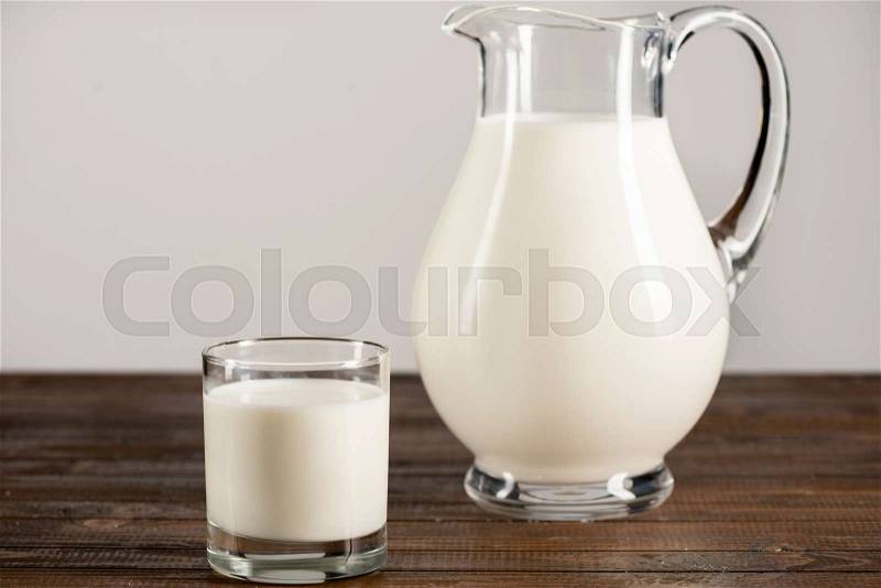 Close-up view of fresh organic milk in glass jug and glass on wooden table top, stock photo