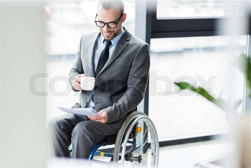 Smiling physically handicapped businessman drinking coffee and looking at documents, stock photo