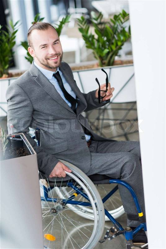 Smiling physically handicapped businessman holding glasses and looking at camera, stock photo