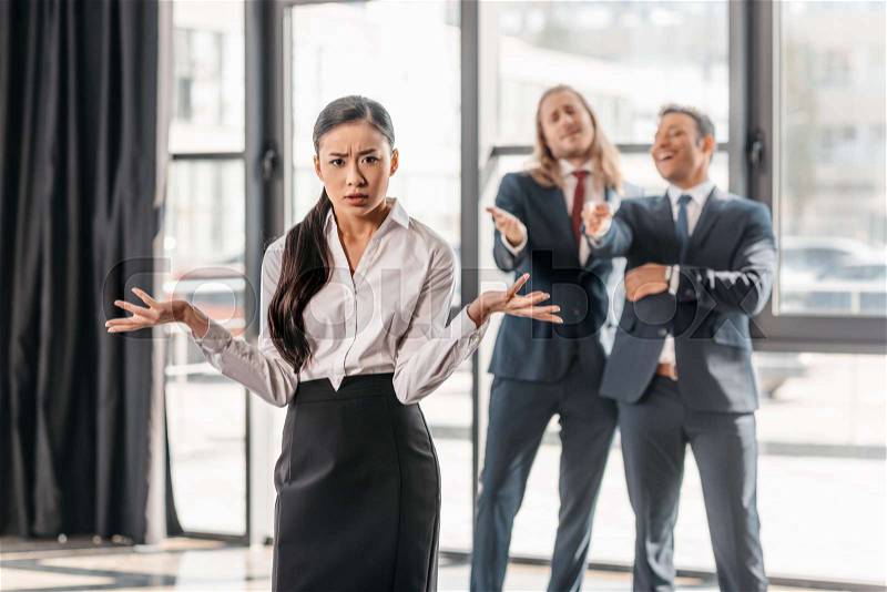 Businesswoman with shrug gesture, businessmen standing behind and laughing, stock photo