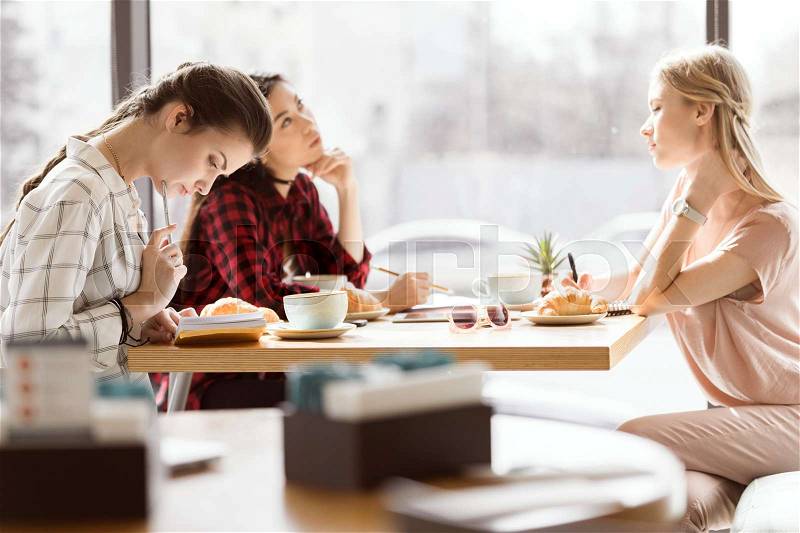 Side view of group of friends study together in cafe, stock photo