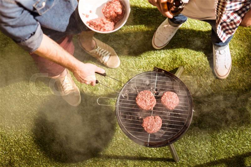 Cropped shot of two young men drinking beer and grilling burgers outdoors, stock photo