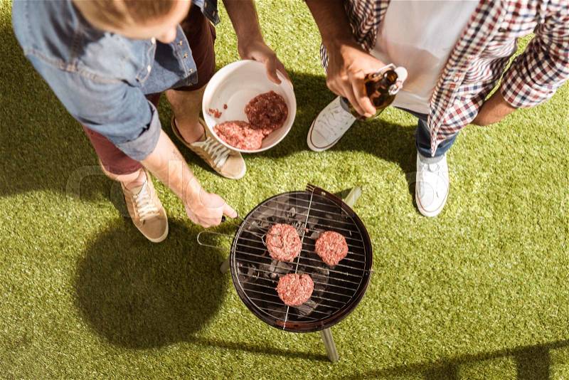 High angle view of young friends grilling burgers on outdoor grill, stock photo