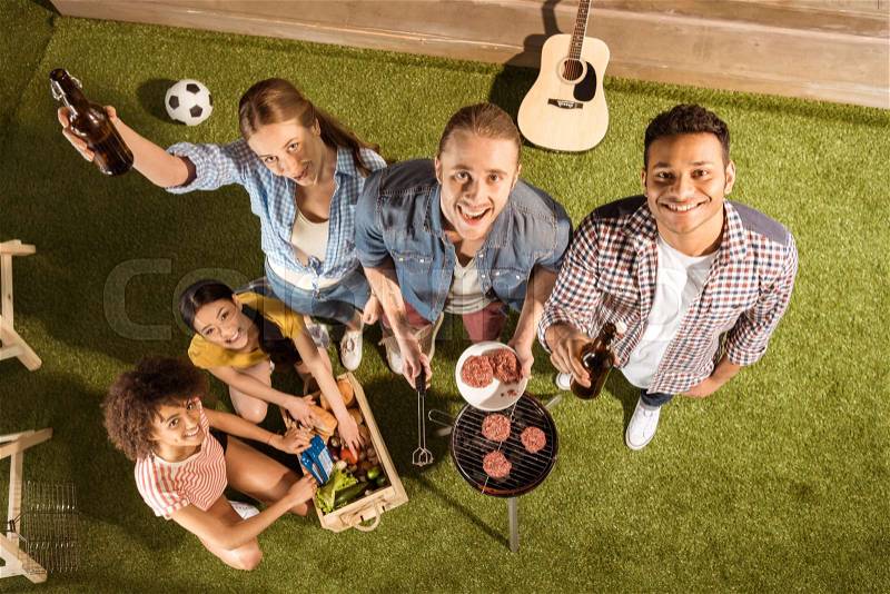 Happy young friends drinking beer and making barbecue smiling at camera, stock photo
