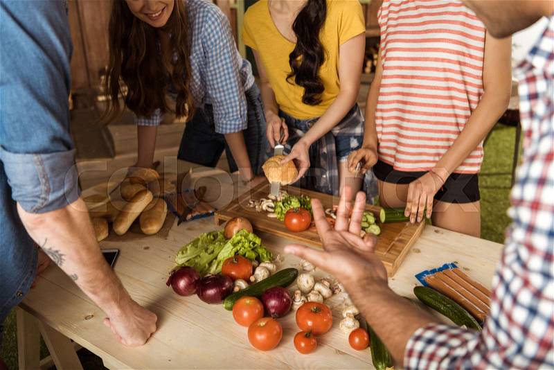 Cropped shot of young friends standing at table and cutting vegetables , stock photo