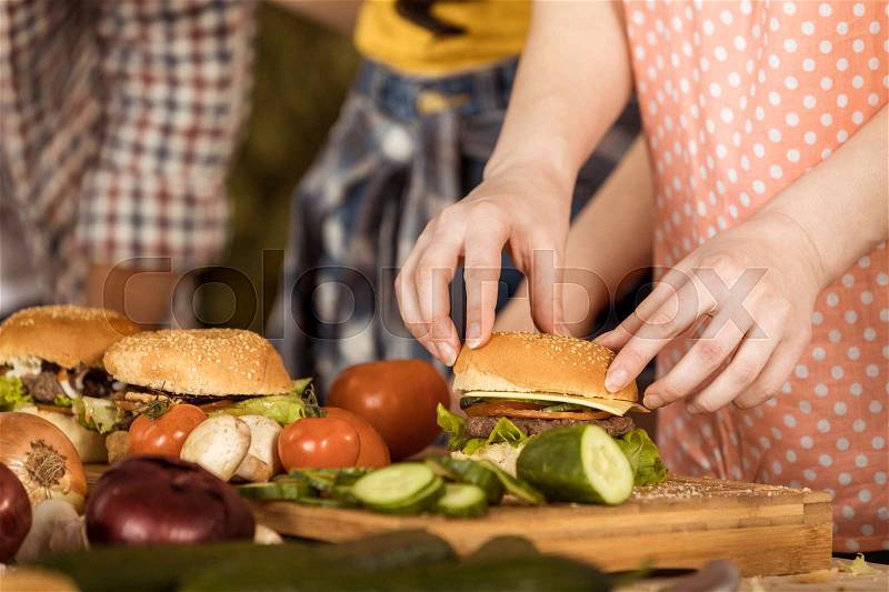 Cropped shot of woman preparing hamburgers for friends on kitchen board, stock photo