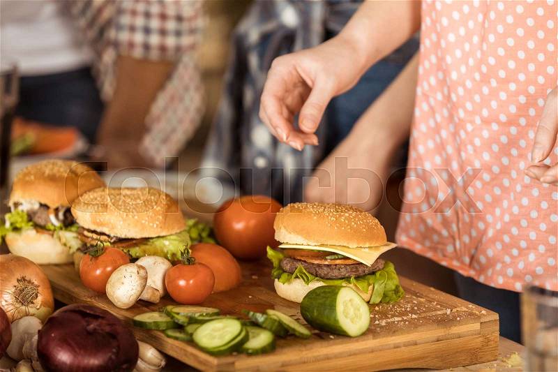 Cropped shot of woman preparing tasty hamburgers for friends on kitchen board, stock photo