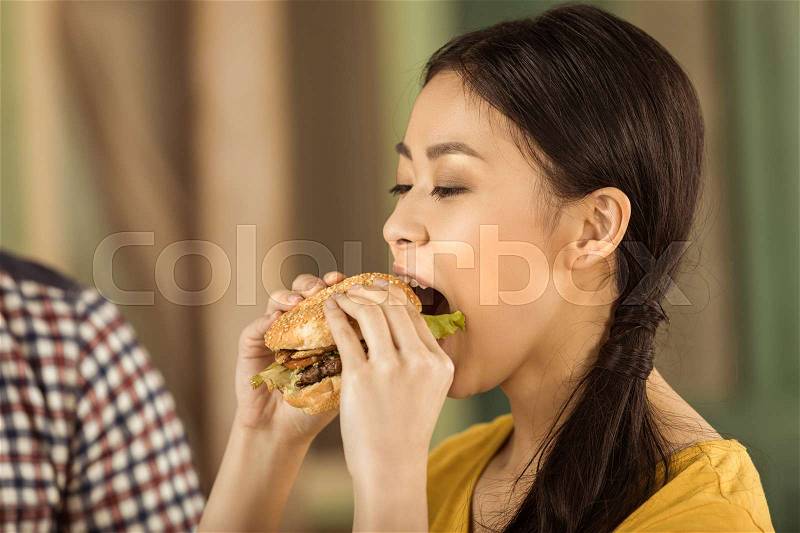 Portrait of young asian girl eating tasty burger, stock photo