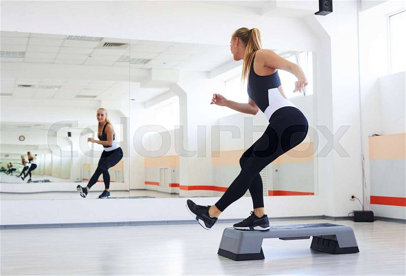 Back view of sporty athlete having a step aerobics in a gym. Woman doing сorner knee step, stock photo