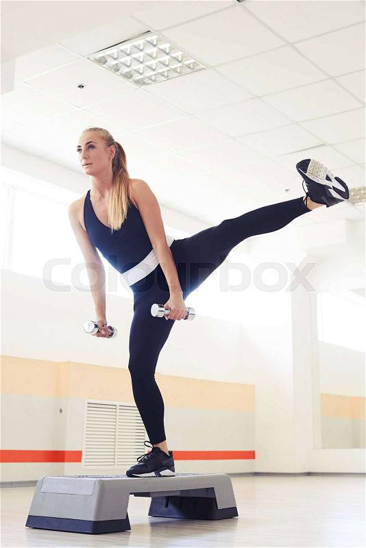 Mid shot of skinny fitness instructor woman working out with dumbbells on a stepper, stock photo