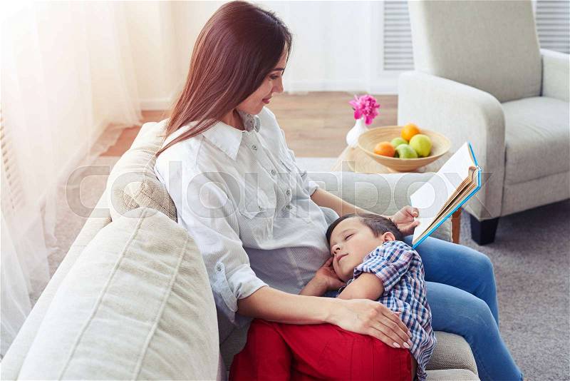 Side view of mother reading a story to her son. Familly sitting in the living room, stock photo