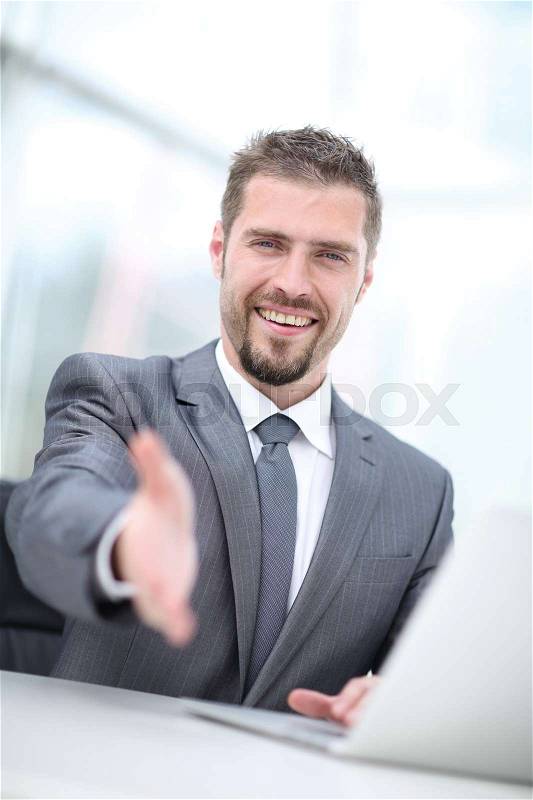 Happy businessman introducing himself holding out his hand in bright office, stock photo
