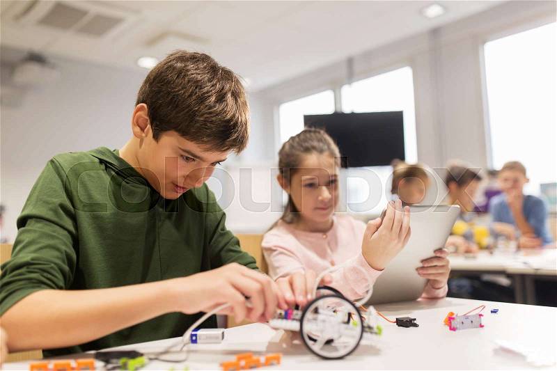 Education, science, technology, children and people concept - group of happy kids or students with tablet pc computer programming electric toys and building robots at robotics school lesson, stock photo