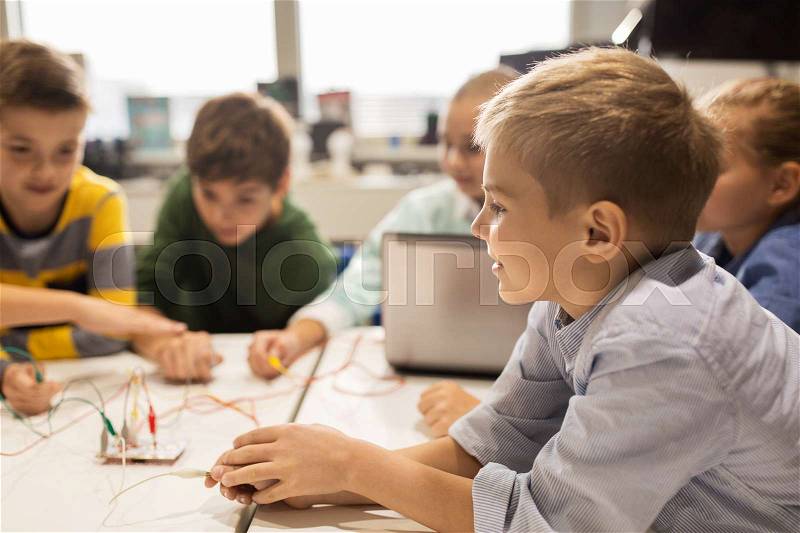 Education, children, technology, science and people concept - group of happy kids with laptop computer playing and invention kit at robotics school lesson, stock photo