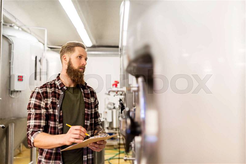 Manufacture, business and people concept - man with clipboard working at craft brewery or beer plant, stock photo