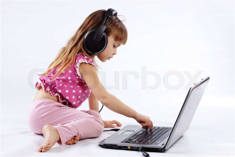 Portrait of funny modern child playing with computer and listening to music in headphones, stock photo