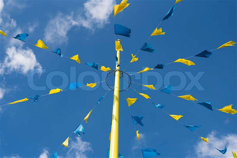 Blue and yellow bunting flags on strings waving in wind at funfair festival against blue summer sky , stock photo