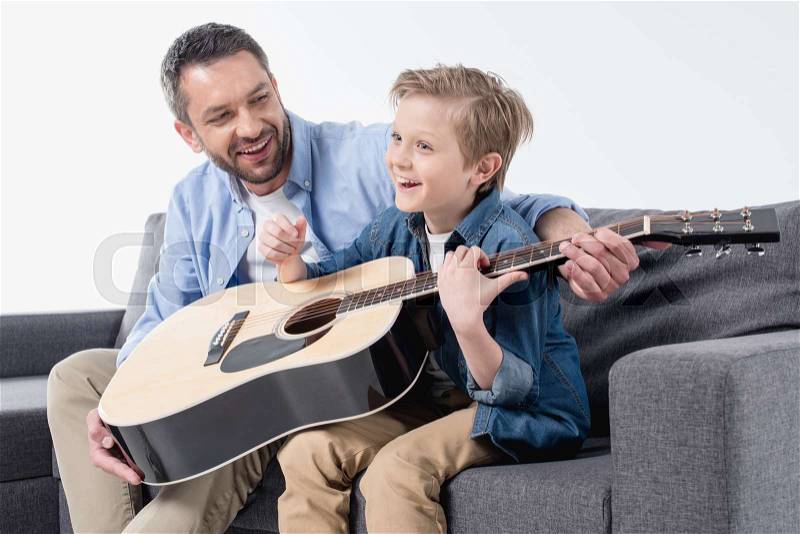 Smiling father teaching his excited son to sing and play on guitar , stock photo