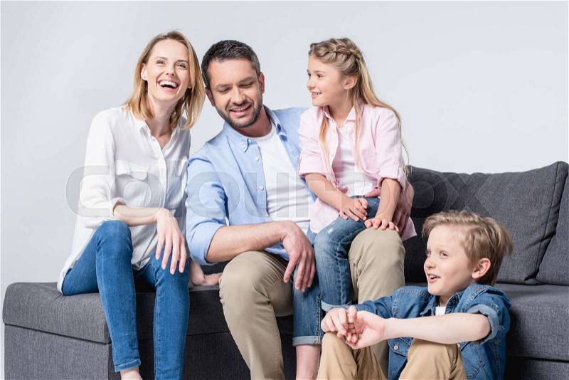 Happy young family with two children sitting together on sofa and smiling, stock photo