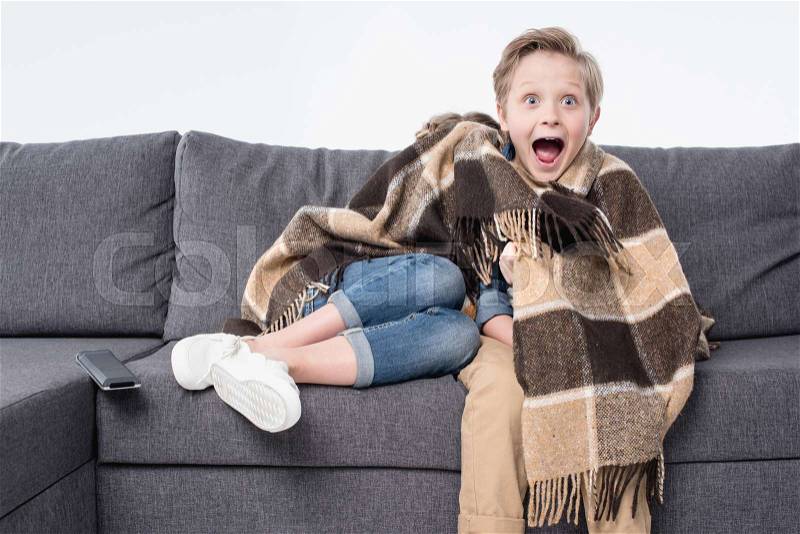 Scared boy watching tv with sister hiding under blanket isolated on white, stock photo