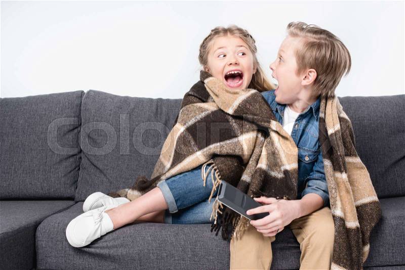 Scared kids in blanket sitting on sofa and looking at each other isolated on white, stock photo