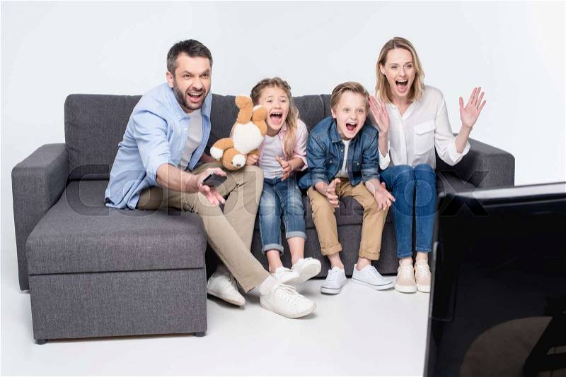 Excited family watching tv while sitting on sofa together, stock photo
