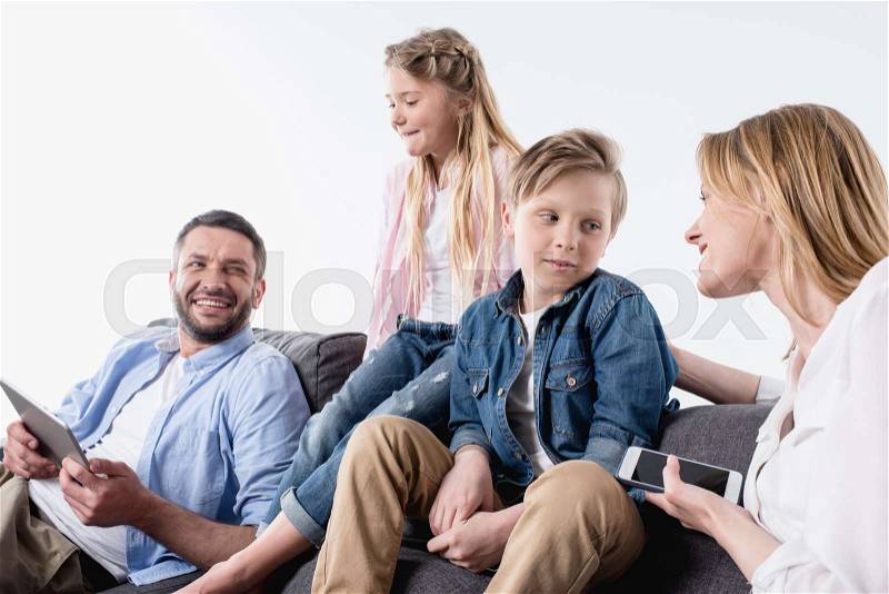 Caucasian family with digital devices sitting on sofa together, stock photo