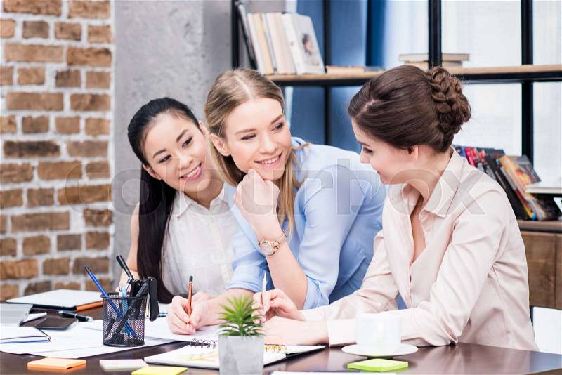 Multiethnic group of young businesswomen working together at table with papers, stock photo
