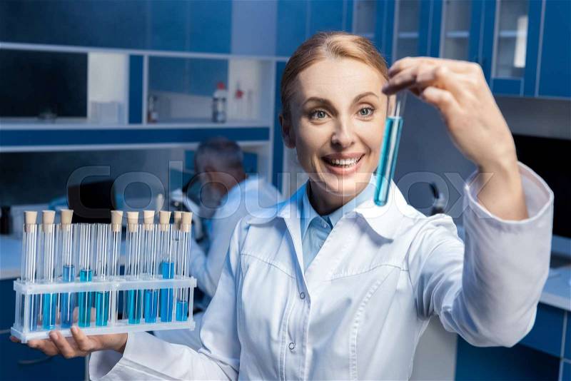 Happy chemist in lab coat holding tubes at laboratory, stock photo