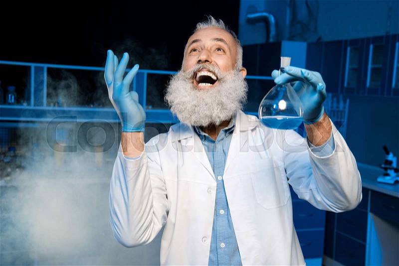 Happy mature scientist in lab coat holding flask with reagent at laboratory, stock photo