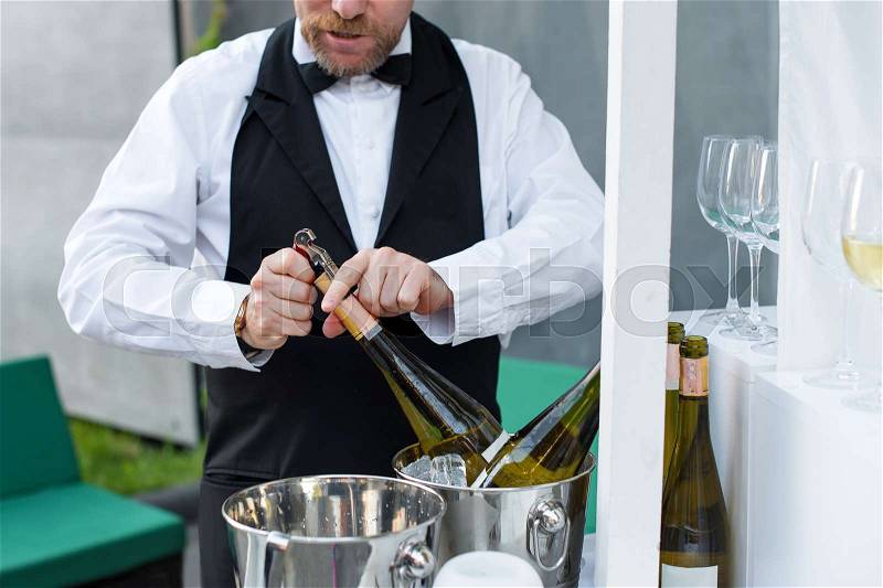 Professional waiter opening bottle of wine with corkscrew, stock photo