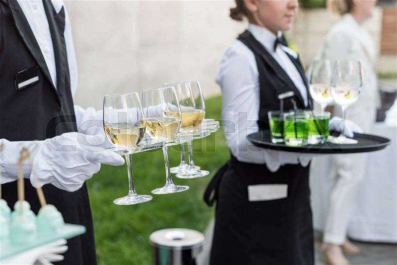 Midsection of professional waiters in uniform serving wine and snacks during buffet catering party, festive event or wedding. Full glasses of champagne on tray, stock photo