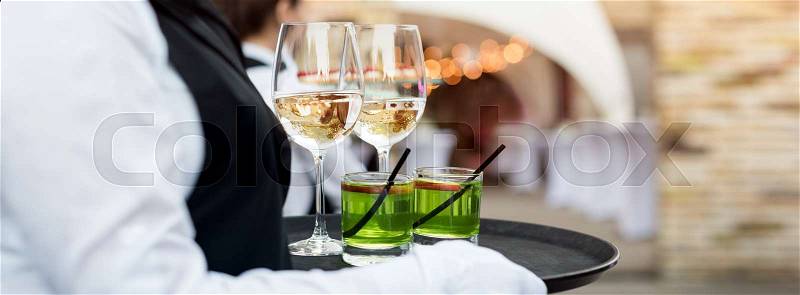 Midsection of professional waiter in uniform serving wine during buffet catering party, festive event or wedding. Full glasses of champagne on tray, stock photo